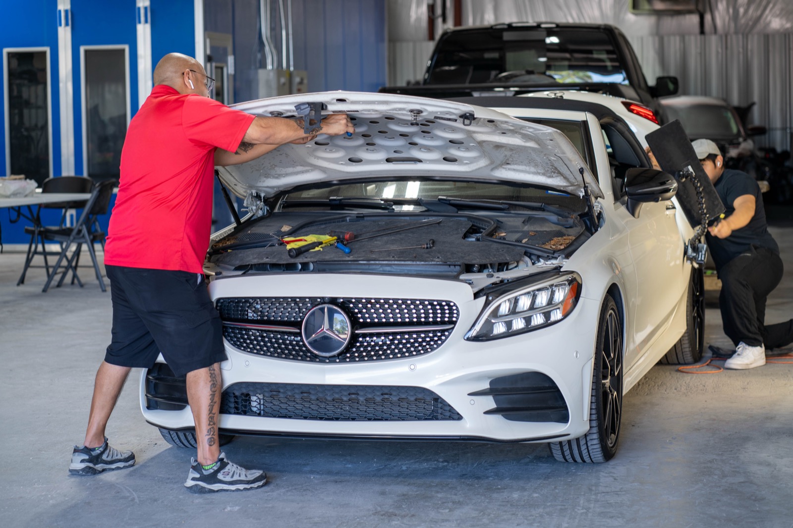 Two AHT techs working on a white Mercedes convertible in the shop bay